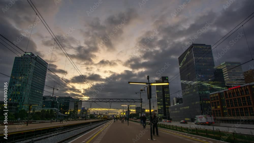 Amsterdam, the Netherlands - oktober 17th 2019: Time lapse of rush hour at the Amsterdam Zuidas train station with cars and trains passing by and commuters walking from the platform to work in offices