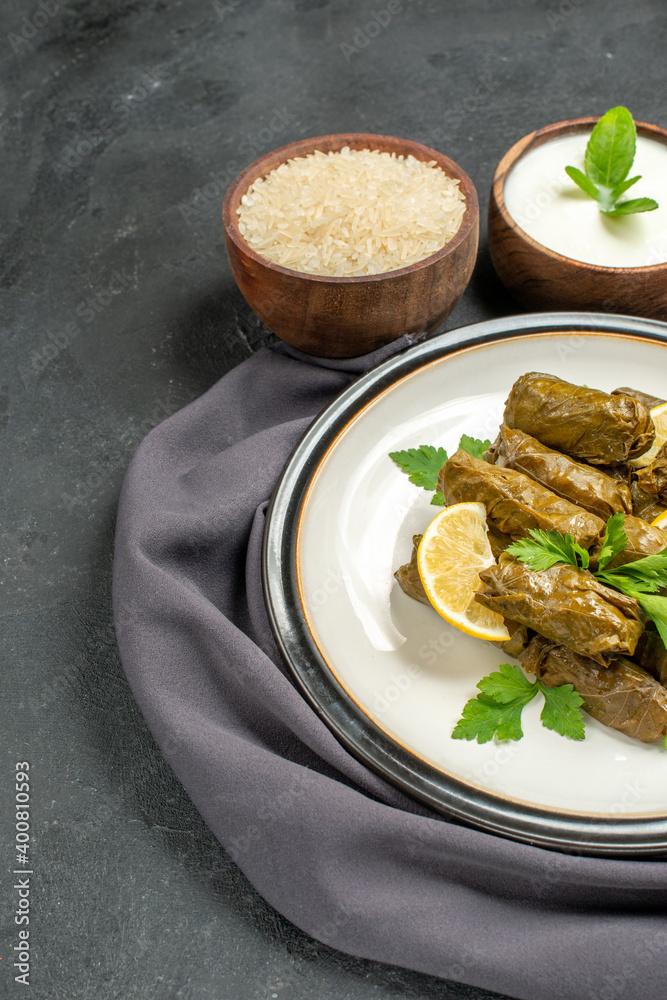 bottom view azerbaijani cuisine dolma in grape leaves on white plate bowls with natural yogurt rice a purple kitchen towel on dark background
