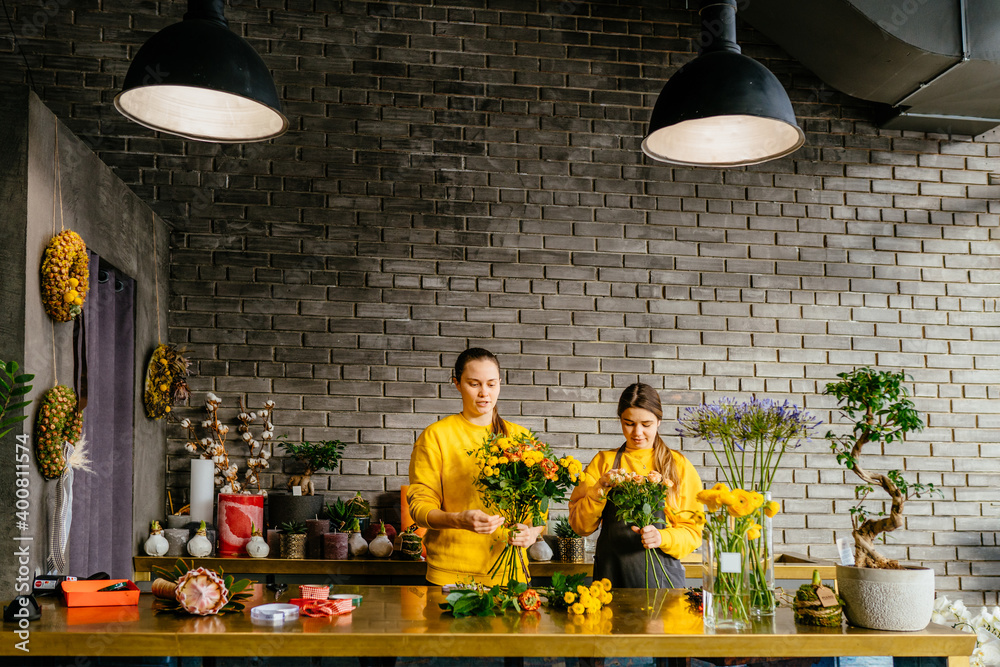 Two smiling florists work in a flower shop. Small business concept. Modern loft interior.