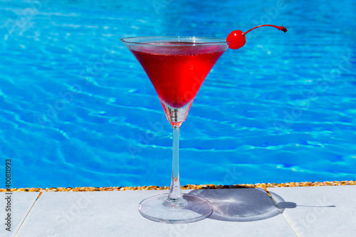 Close up glass of cosmopolitan cocktail decorated with a cherry on the edge of the infinity pool in the hotel. Tropical vacation concept. photo