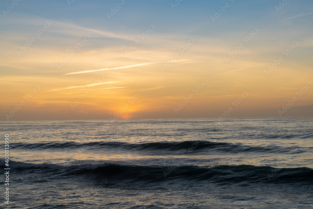 sunset over the ocean with colorful sky and large waves rolling in towards the coast