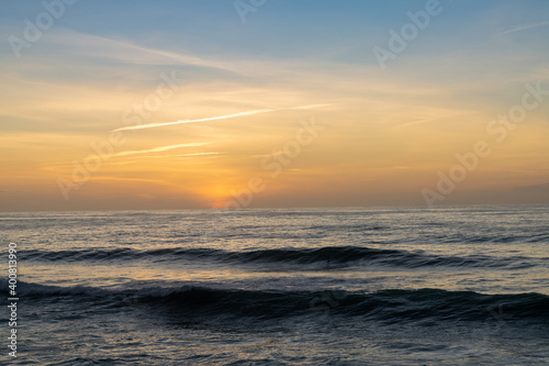 sunset over the ocean with colorful sky and large waves rolling in towards the coast
