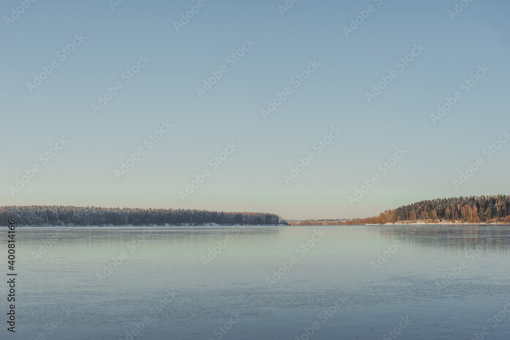 Frozen lake, clear transparent ice and frozen trees in a forest without foliage.
