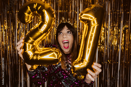 .Beautiful woman dressed for New Years Eve in a sparkling dress. Fun and festive attitude. Holding metallic balloons. Year 2021