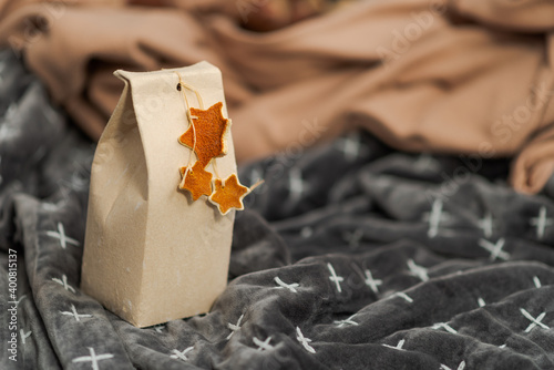 Selfmade gift box out of old beverage carton decorated with star shaped cut out dried roange peel standing on rumpled blankets on couch photo