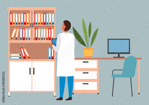 Man is standing with a clipboard or tablet. Male doctor looking at the bookcase with documents. Hospital worker spends time in the medical institution. The doctor works with paper and documentation