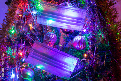 Medical masks on the Christmas tree illuminated with colored lights garlands.