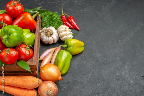 Side view of fresh various organic vegetables inside and outside of a wooden basket on dark background