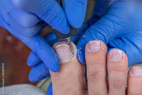 The nail technician processes the cuticle on the toe. Hardware pedicure in the salon.