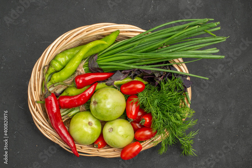 A vegetable basket with a bunch of green and peppers cucumber and tomatoes with stem on dark background