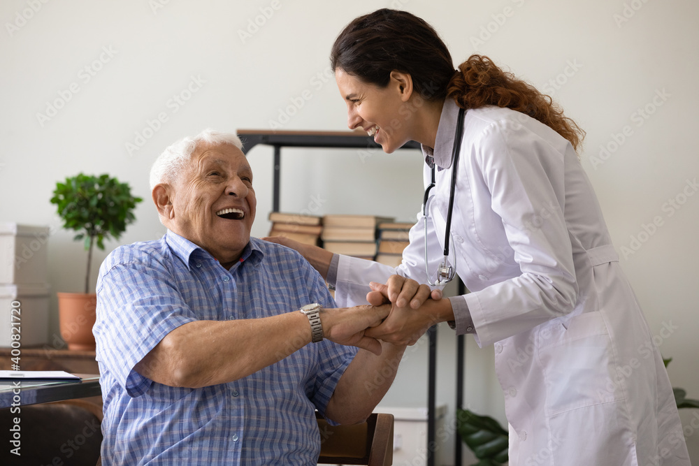 Positive young female nurse have fun laugh and joke with happy elderly male patient at consultation in hospital. Caring woman doctor support cheer and comfort mature man. Good medicine concept. - obrazy, fototapety, plakaty 