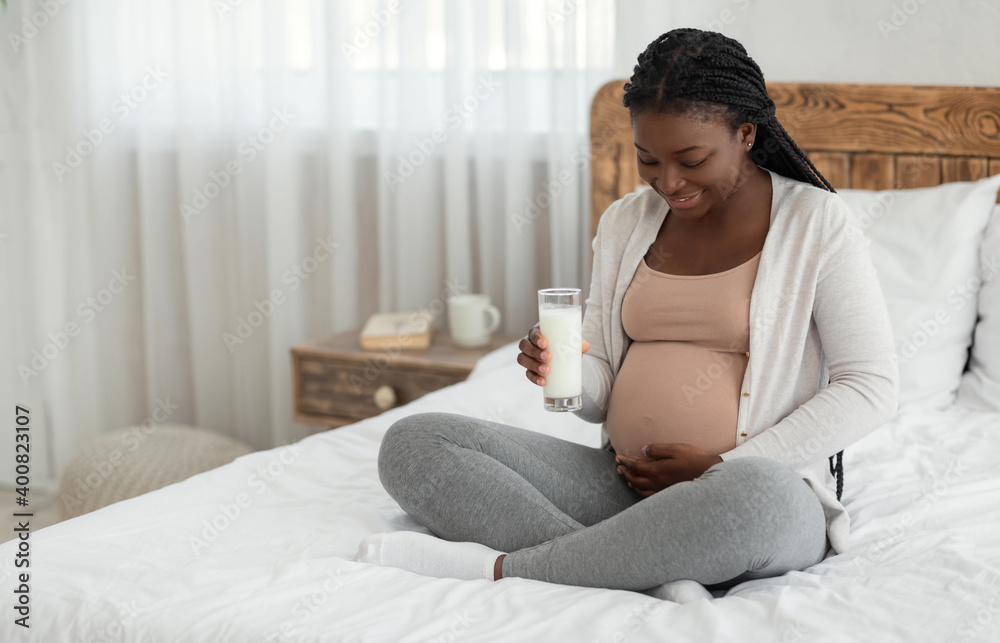 Smiling black pregnant woman drinking glass of fresh milk at home Smiling black pregnant woman drinking glass of fresh milk at home