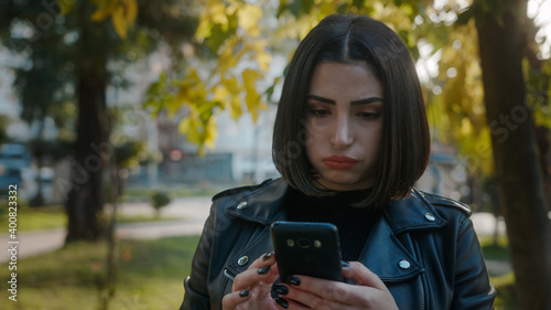 Young unhappy pretty woman wearing a leather jacket is dealing with the phone.