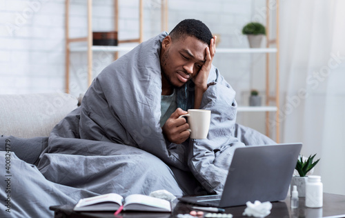 Bild auf Leinwand Sick African Man Using Laptop Having Fever And Headache Indoor