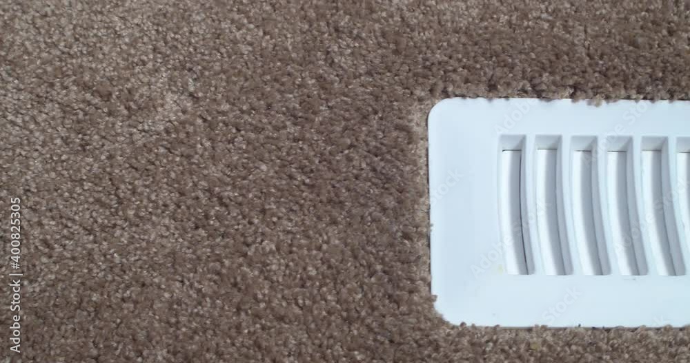 A person opening a hot air coming vent inside residencial home, hot air vent on a brown carpet.