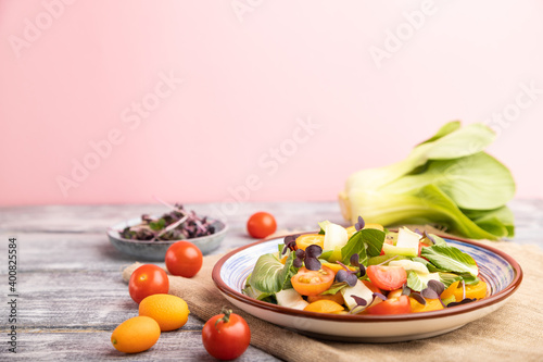 Vegetarian salad of pac choi cabbage, kiwi, tomatoes, kumquat, microgreen sprouts on gray wooden background. Side view, selective focus, copy space.