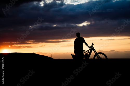 A man's silhouette with his bike in a beautiful sunset background.