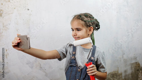 Girl repairing room, painting the wall with white color and making selfie on smartphone