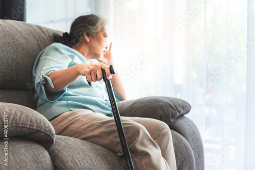 Close up images, Hand of Asian elderly woman Which holds the cane to support, Sitting absent lonely on the sofa and looking outside the door, to health care and retirement age concept.