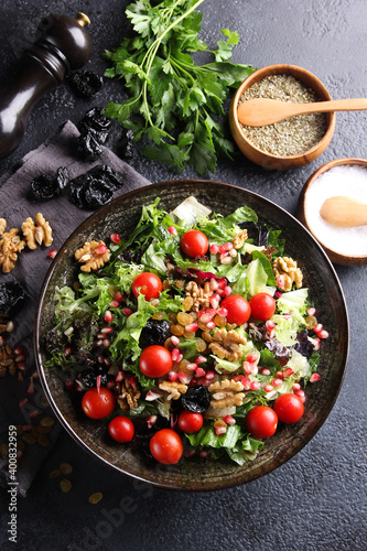 Oriental cuisine. Bright vegetable salad with nuts, tomatoes, prunes, lettuce, corn and cheese in a grey plate on a black table. Restaurant menu, top view, flatlay, copy space, vertical