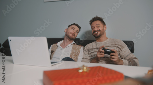Happy gay couple or best friends playing video games. Gift in the foreground. High quality photo