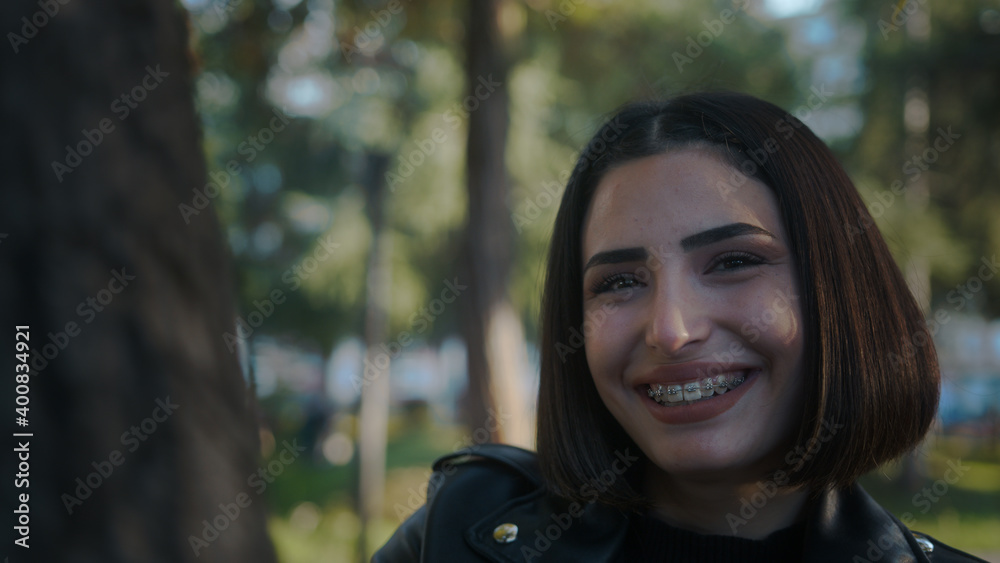 Young girl wooing her lover behind the tree. Smiling young cheerful woman with braces. Young girl wooing her lover behind the tree. Smiling young cheerful woman with braces.