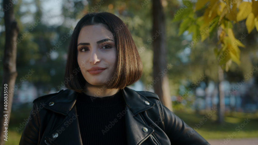Portrait of young beautiful woman in black jacket with short hair posing on camera in park. Sunny good weather Portrait of young beautiful woman in black jacket with short hair posing on camera in park. Sunny good weather