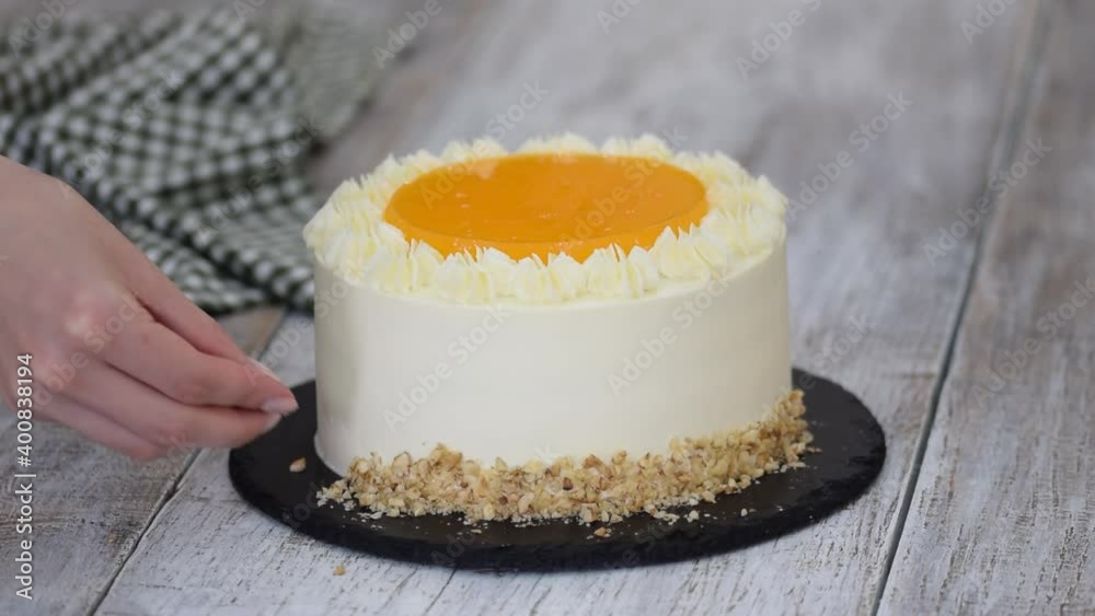 Woman decorates carrot cake with chopped walnuts.