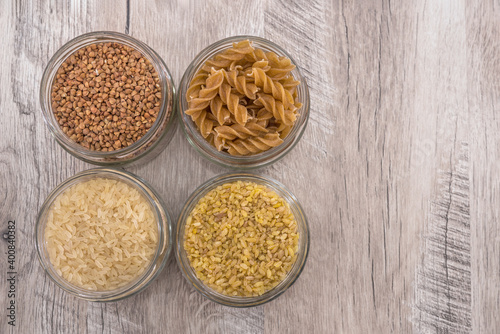 buckwheat, rice, pasta and bulgur in jars on a wooden background.