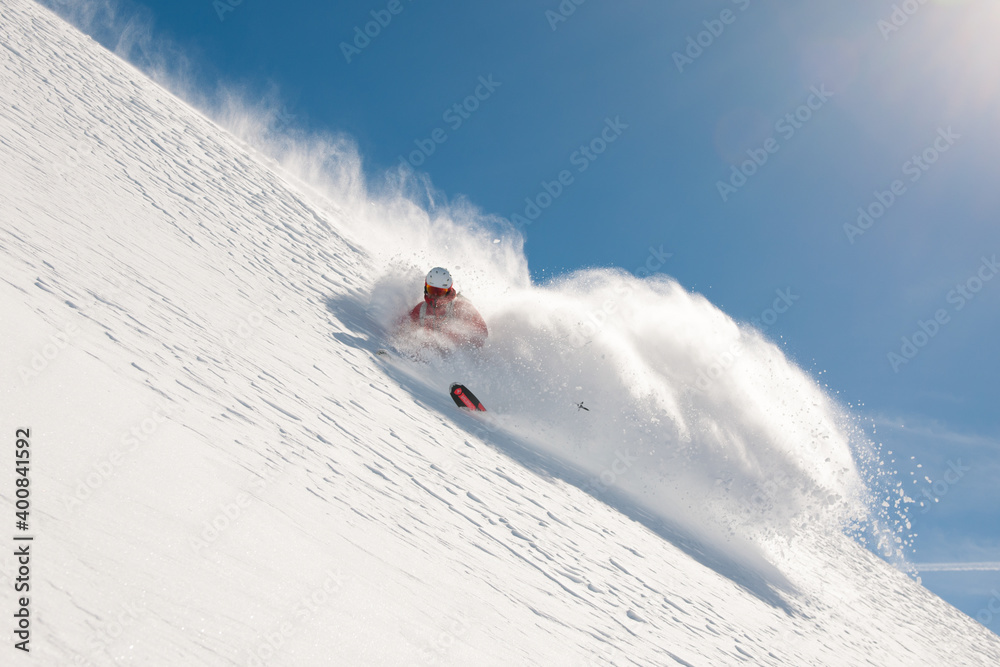 Fototapeta premium Freeride skier going fast downhill. Stock picture of a freeride skier that is skiing fast downhill in deep powder snow. There is a beautiful clear blue sky in the background. The location is Hochgurgl