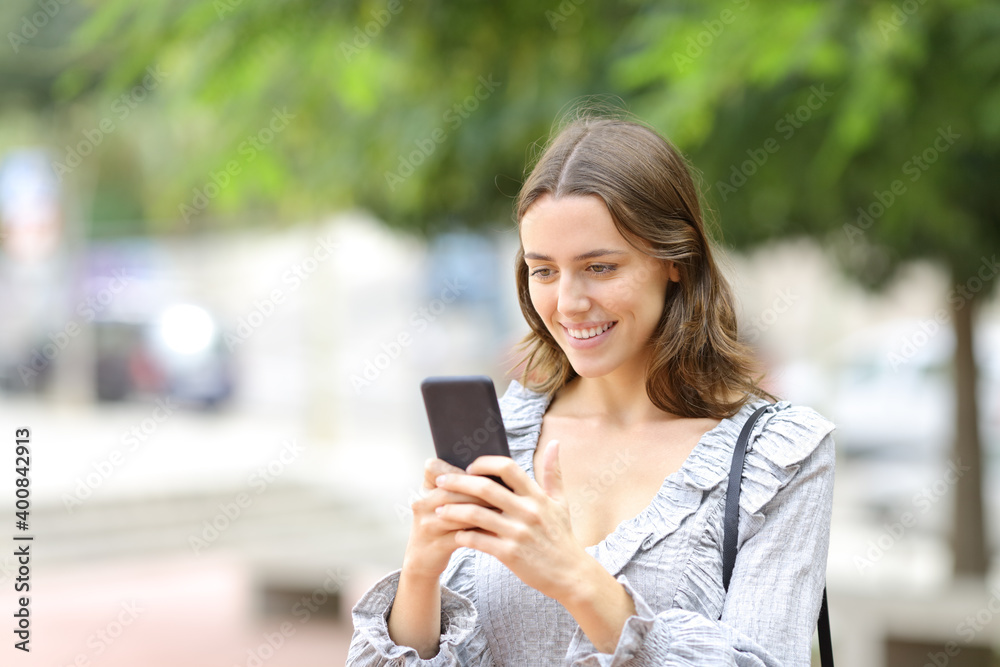 Happy teen texting on phone walking in the street