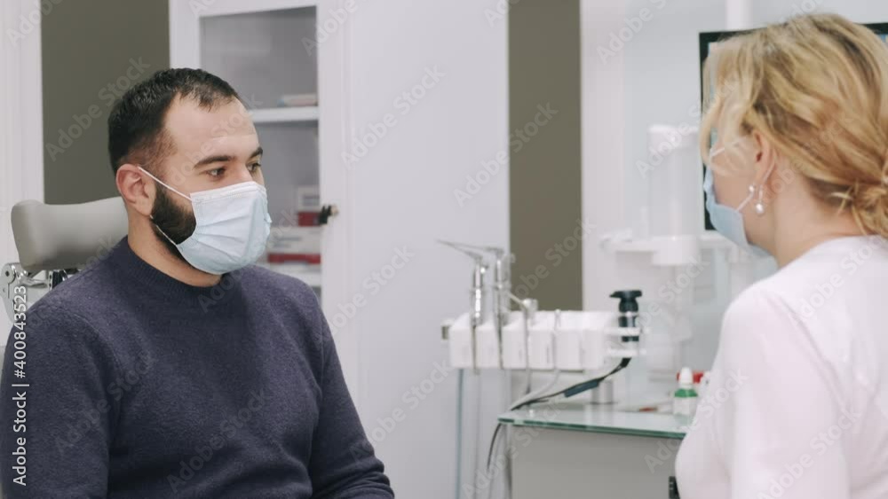 Female otolaringologist and male patient sitting in doctor's cabinet. The man is suffering from throat and nose problems. The doctor is talking to her patient.