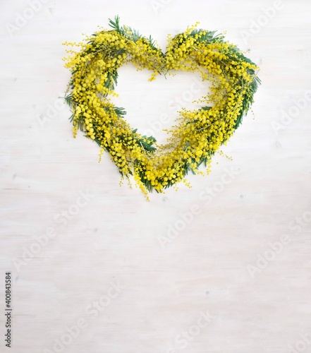 spring mimosa flowers wreath in heart shape on white wood background. Vertical image  with copy space. Women day, mothers day, spring card concept
