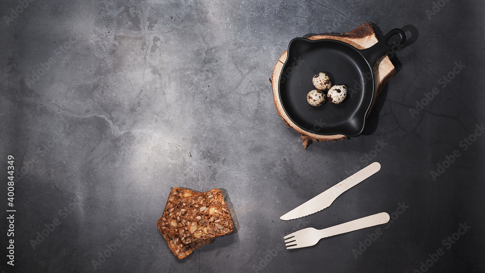 Raw quail eggs in a black round pan, next to bread and a disposable wooden fork and knife. The view from the top Raw quail eggs in a black round pan, next to bread and a disposable wooden fork and knife. The view from the top