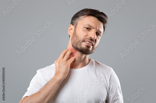 Bearded man scratching neck on grey background, having annoying itch photo