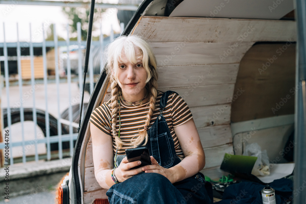 Young woman sitting in back of van with phone Young woman sitting in back of van with phone