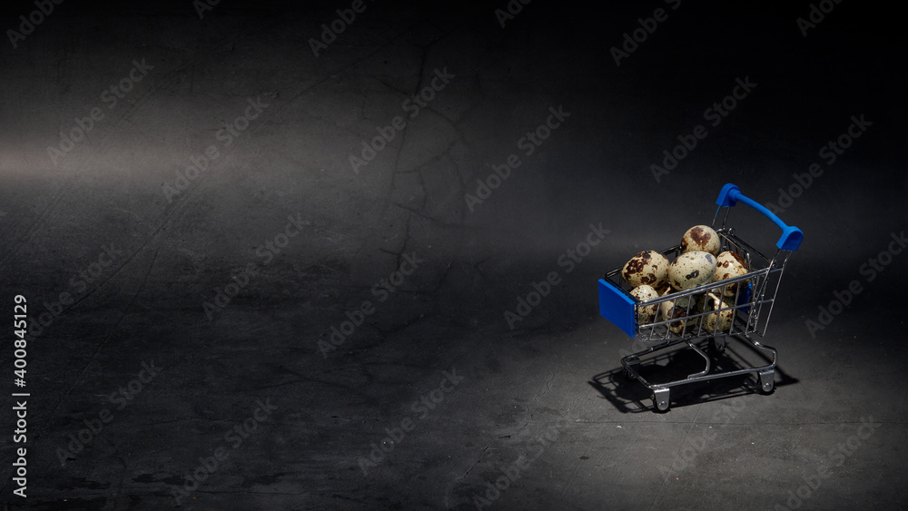 Quail eggs in a miniature supermarket cart on a dark background. advertising concept of consumerism. Go grocery shopping. Place for your text Quail eggs in a miniature supermarket cart on a dark background. advertising concept of consumerism. Go grocery shopping. Place for your text