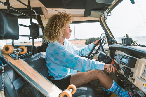 Young blond Afro woman sitting by skateboard while driving old off-road vehicle photo