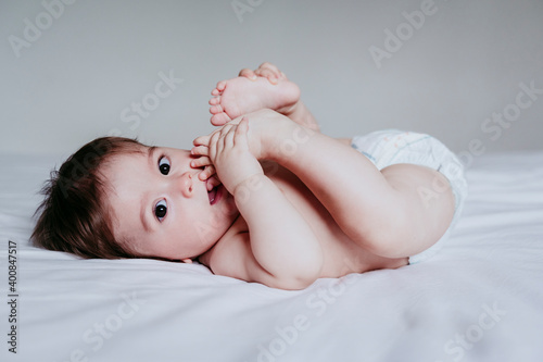 Cute baby boy putting foot in mouth while lying on bed at home