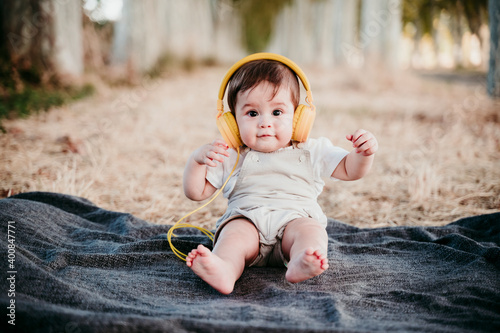 Cute baby boy wearing headphones while sitting on blanket outdoors