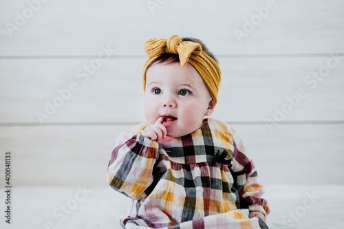 Baby girl with finger in mouth sitting on bed at home