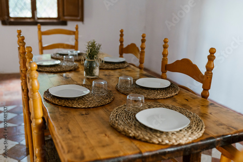 Place setting on wooden dining table with empty chairs in room