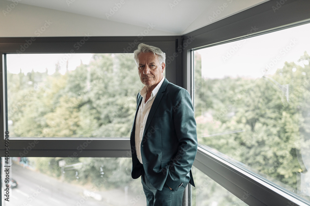 Businessman with hand in pockets standing by window at office Businessman with hand in pockets standing by window at office