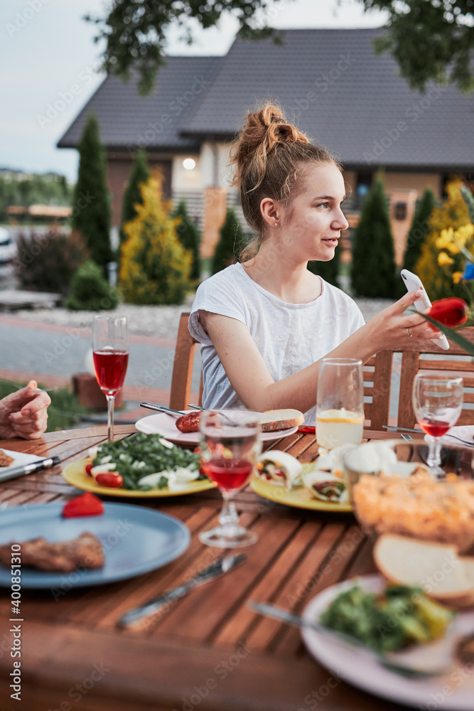 Family having a meal from grill during summer picnic outdoor dinner in a home garden. Close up of people sitting at a table with food and dishes
