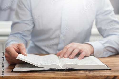 Open book Bible. The man leafs through the pages of the book. Sitting at the table he reads.