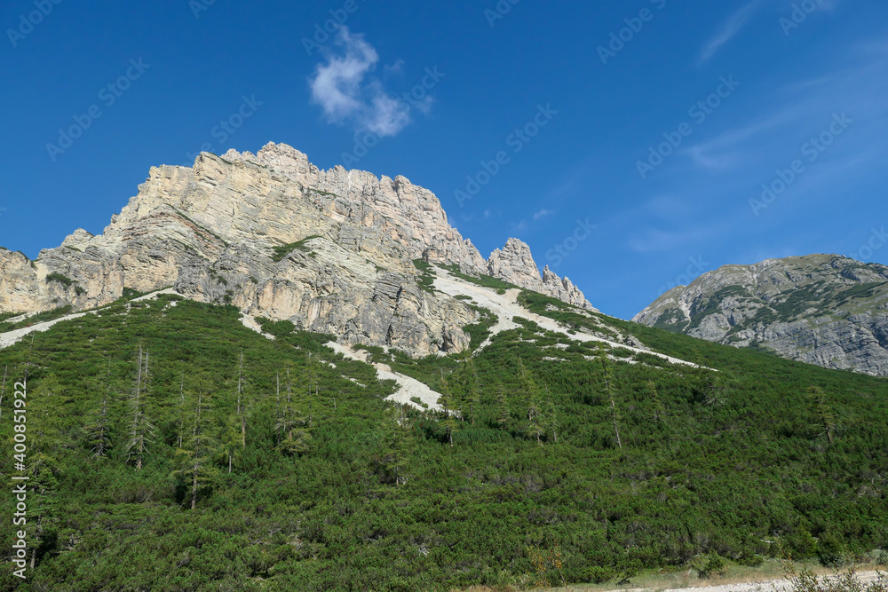 A distant view on a high mountain in Italian Dolomites. It has very steep slopes, full of landslides and lose stones. Thick forest at the foothill of the mountain. High mountaineering. Experience