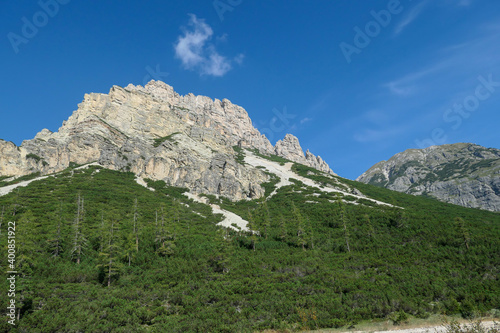 Fototapeta Naklejka Na Ścianę i Meble -  A distant view on a high mountain in Italian Dolomites. It has very steep slopes, full of landslides and lose stones. Thick forest at the foothill of the mountain. High mountaineering. Experience