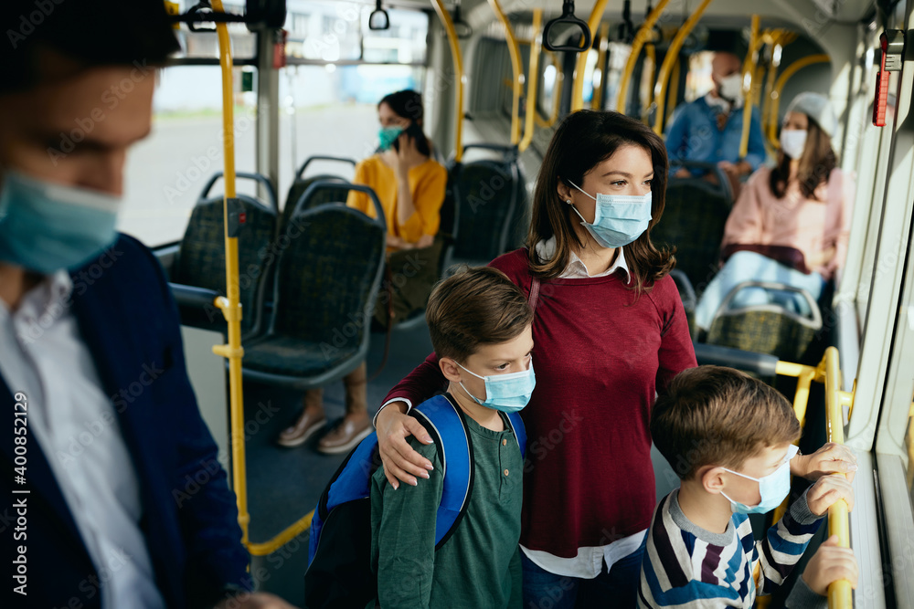 Mother and her sons wearing protective face masks while commuting by bus.