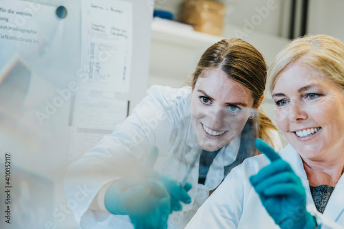 Smiling scientist and assistant discussing while examining human brain microscope slide at laboratory