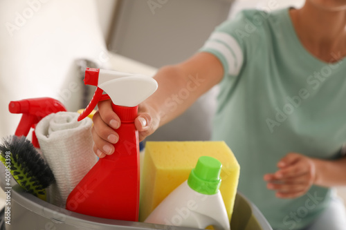 Woman taking bottle of detergent from bucket with cleaning supplies indoors, closeup